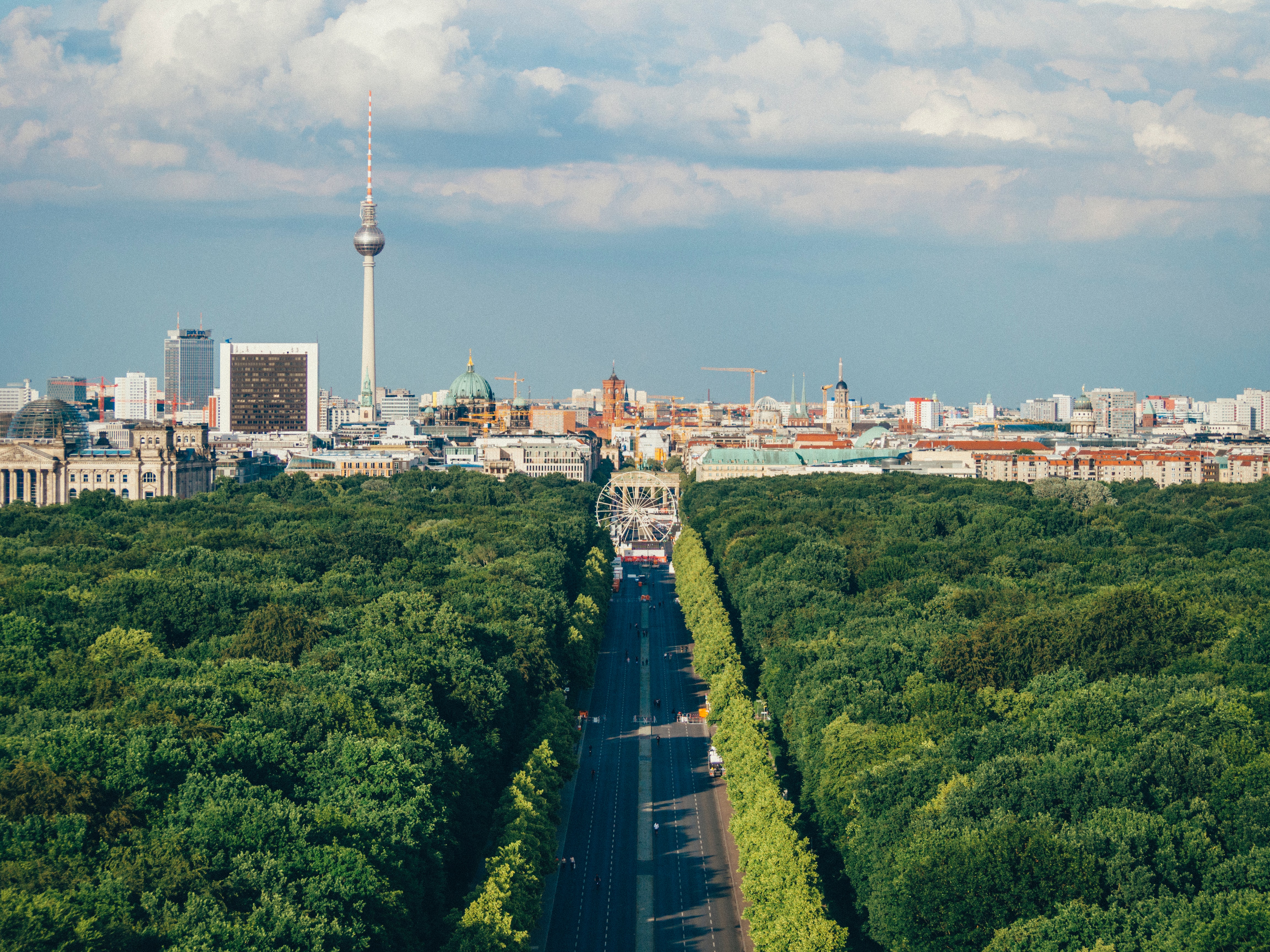 Aerial view of the city of Berlin, with a road dividing a forest leading to the buildings in the city.